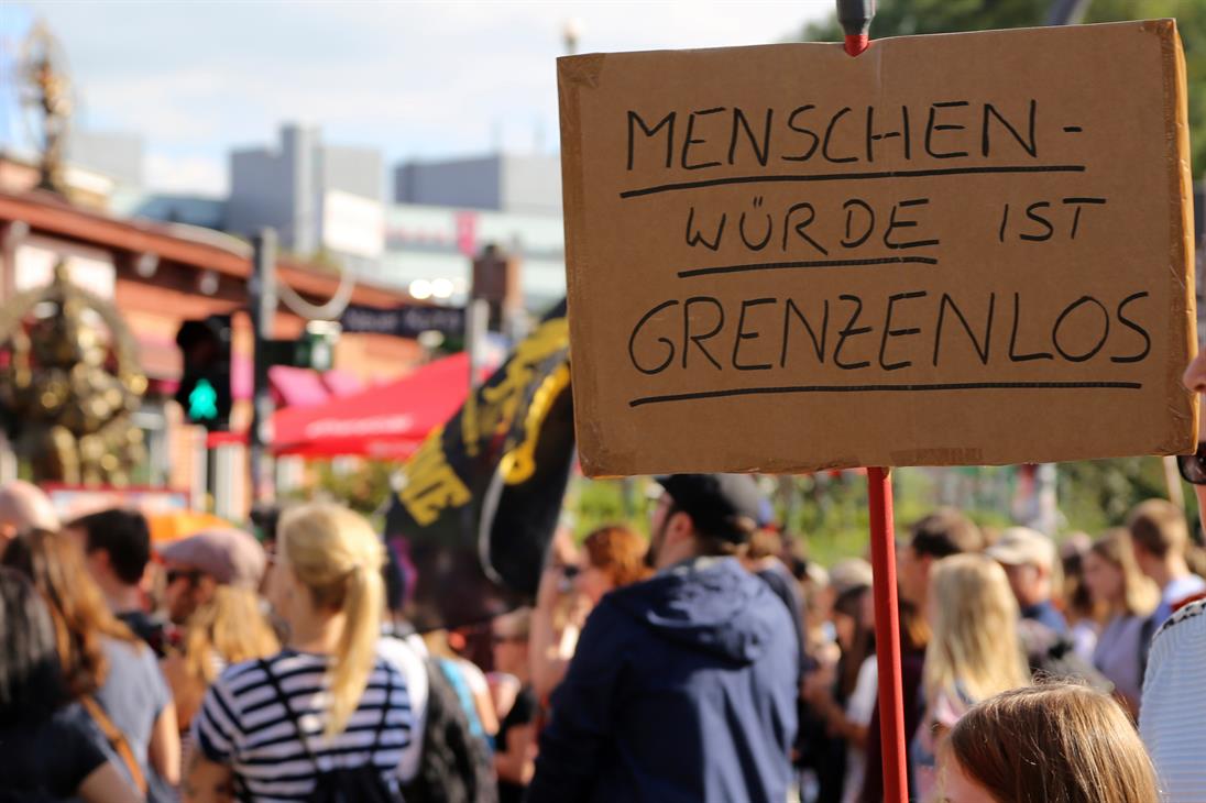 Ein Foto von Menschen bei einer Demonstration. Im Fokus ist ein Schild mit der Aufschrift: "Menschenwürde ist grenzenlos"